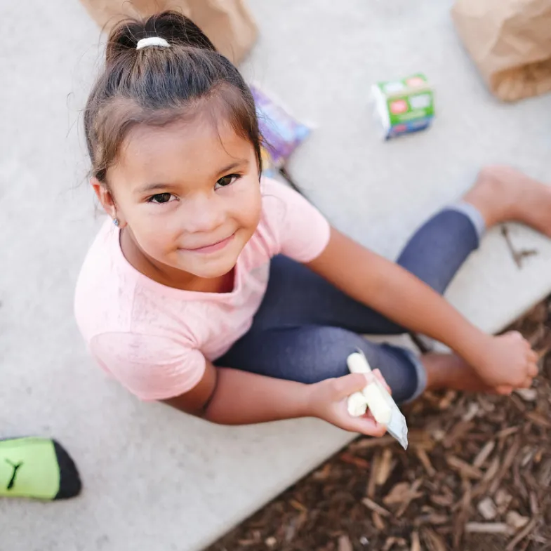 Little girl looking up at camera and eating a cheese stick