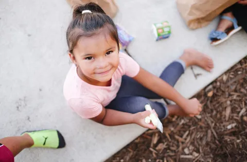 Little girl looking up at camera and eating a cheese stick